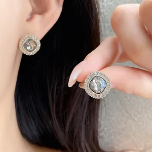 Dettaglio di eleganti orecchini a perno con cristallo quadrato e strass sull'orecchio.