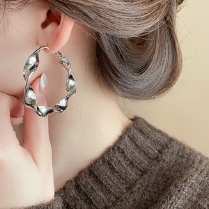 Close-up view of twisted silver spiral hoop earring worn on model's ear for fashion