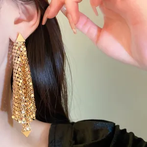 Gros plan de boucles d'oreilles pendantes à pompons dorés et clous triangulaires