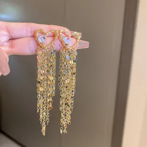 Gros plan de boucles d'oreilles cœur dorées avec de longs glands de paillettes brillants