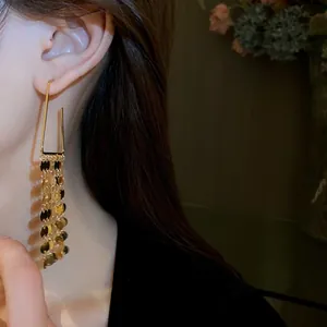 Gros plan élégant de boucles d'oreilles losanges dorées avec de longs glands à paillettes au lobe