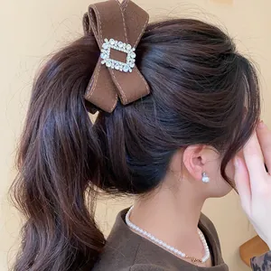 Detail view of an elegant brown fabric bow banana clip with sparkling rhinestone buckle on hair