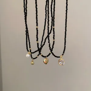 Détail de colliers en perles noires avec pendentifs coeur doré et cristal