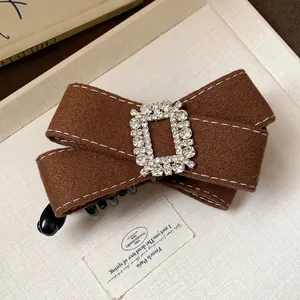 Close-up detail of brown fabric bow hair clip with elegant sparkling rhinestone buckle.