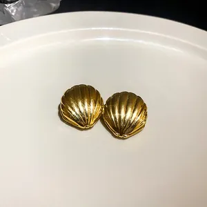 Makroansicht goldener Muschel-Ohrstecker mit gerippter Textur auf weißem Teller