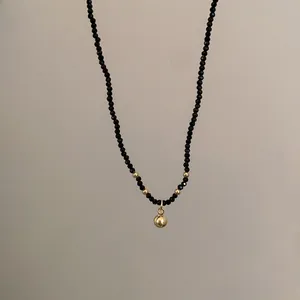Gros plan d'un collier minimaliste en perles noires avec billes dorées et pendentif sphère.