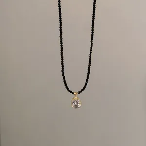 Détail du collier de perles noires avec pendentif en cristal carré et monture dorée.