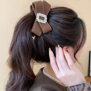 Elegant brown fabric bow hair clip with rhinestone buckle worn on a ponytail