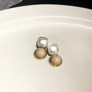 Detail eleganter geometrischer goldener Ohrringe mit weißen quadratischen und beigen Perlen
