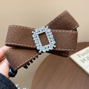 Detailed close-up of a brown fabric bow hair clip featuring a sparkling rhinestone buckle.