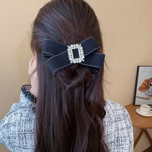 Back view of an elegant black fabric bow hair clip with rhinestones on a woman's hair