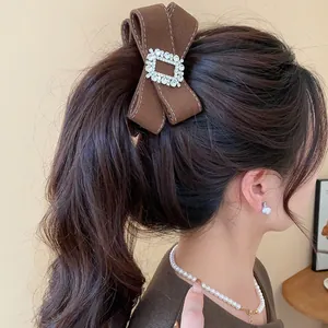 Close-up view of an elegant brown rhinestone bow banana hair clip styled on a model's ponytail