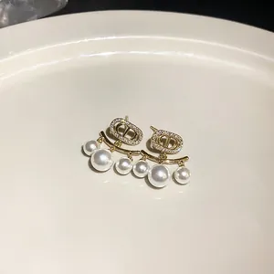 Elegante goldene Ohrringe mit dem CD-Logo, Zirkonsteinen und hängenden Perlendetails