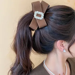 Detailed view of an elegant brown fabric bow hair clip with a rhinestone buckle on hair