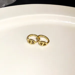 Detailansicht goldene geometrische Creolen mit Schweinenase-Glied-Design auf weißem Teller