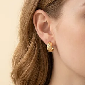 Elegantes pendientes de aro dorados en forma de C con textura de trama cruzada en la oreja.