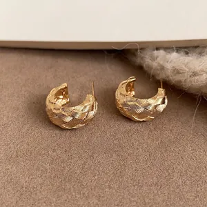 Primer plano detallado de pendientes en C dorados con una elegante textura cruzada tejida