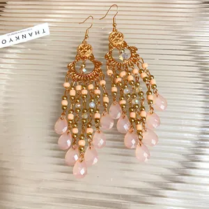 Dettaglio di orecchini pendenti bohémien con eleganti perline di vetro rosa e oro.