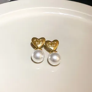 Makro-Detail von eleganten goldenen Herz-Ohrringen mit weißen Perlen auf Keramikgrund.