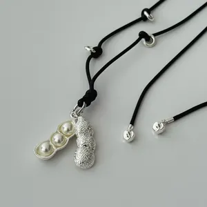 Minimalist peanut and pea pod pendant necklace with white pearls on a long black cord.
