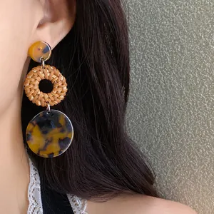 Detailed view of boho woven rattan and tortoiseshell resin drop earrings on model.