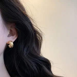 Elegantes pendientes dorados en forma de C con textura cruzada tejida en una modelo
