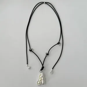 Detail view of the pea pod pendant with three pearls on a black cord sweater chain.
