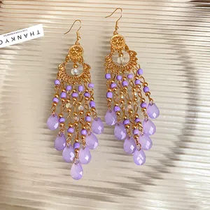 Dettaglio di orecchini boho con nappe, perline viola e pendenti a goccia d'acqua