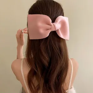 Detailed rear view of a large elegant pink fabric bow hair clip on long brown wavy hair