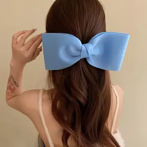 Macro view of an oversized light blue fabric bow hair clip on long wavy brown hair