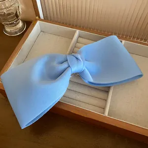 Close-up detail of a minimalist light blue fabric bow hair clip in a wooden jewelry box.