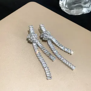 Close-up of silver-plated tassel earrings with sparkling baguette zircons and knot design.