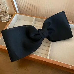 Elegant close-up of a large black fabric bow hair clip inside a wooden jewelry box.