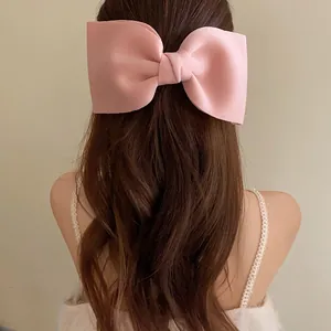 Detailed view of an oversized pink fabric bow hair clip on long wavy brown hair