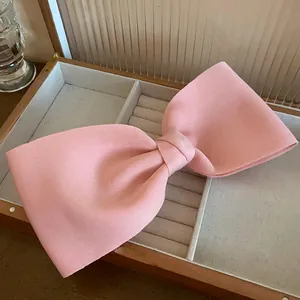Detailed macro shot of a soft pink fabric bow hair clip inside a wooden jewelry box.