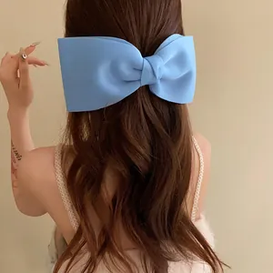 Rear view of a model wearing a light blue oversized bow hair clip on long wavy brown hair