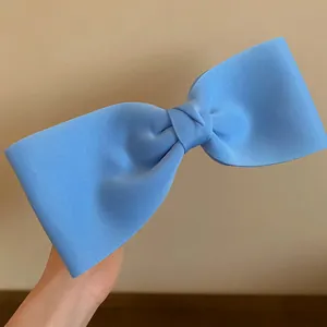 Detail of a light blue oversized fabric bow hair clip with textured ribbed surface finish.