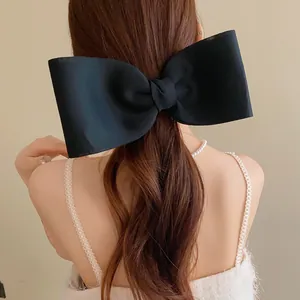 Elegant large black silk bow hair clip accessory shown on model's hair from behind