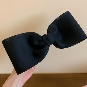 Close-up detail of a large black fabric bow hair clip with elegant stiff texture