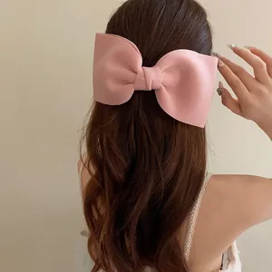 Detailed view of an elegant large pink fabric bow hair clip on long wavy brown hair.