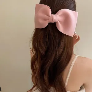 Detailed back view of an elegant oversized pink bow hair clip on long wavy brown hair