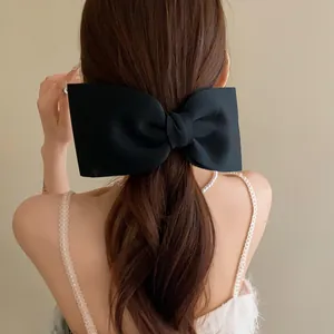 Detailed view of a large black fabric bow hairclip styled on long wavy brown hair
