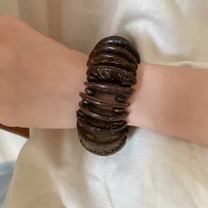 Detailed view of a dark brown bohemian coconut shell disc bracelet worn on a wrist.
