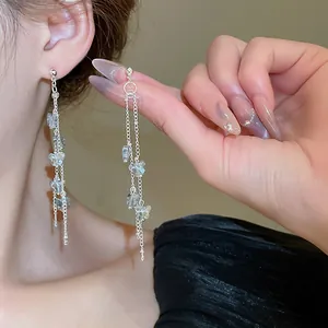 Close-up of delicate Korean-style tassel earrings with blue flower charms worn on ear.