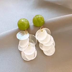 Close-up of elegant green stud earrings with white cascading shell disc tassels