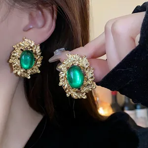 Close-up detail of vintage oval earrings with green gemstone and gold leaf frame