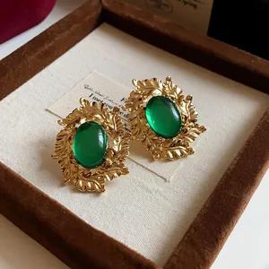 Close-up of vintage emerald green oval stud earrings with ornate gold leaf frame