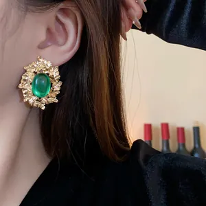 Macro view of vintage gold leaf stud earring with green oval stone worn by model
