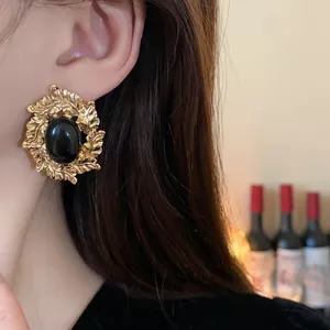 Detail view of vintage baroque gold leaf earrings with a black oval stone on a model.