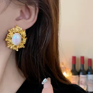 Close-up view of vintage gold leaf stud earrings with oval pearl detail on model's ear.